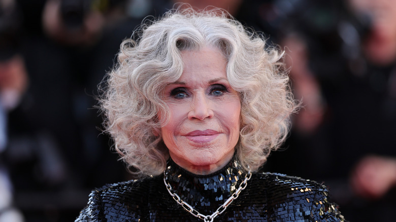 Jane Fonda wears a sparkly black gown rocks voluminous gray curls while standing in front of a blurred background at a red carpet event.