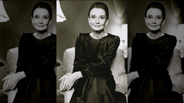 Audrey Hepburn posing for a portrait wearing a black long-sleeve satiny dress.