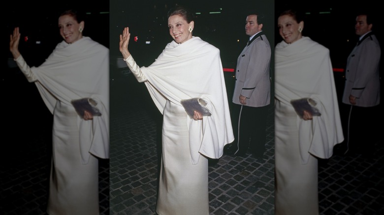 Audrey Hepburn at the Golden Globes wearing a white dress with a white shawl wrap, waving at the cameras.