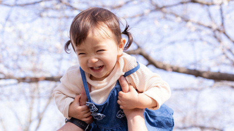 Family holding up baby daughter under cherry blossoms
