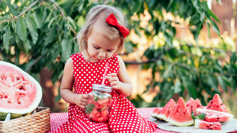 Cute child eats ripe juicy watermelon at summertime. Child, baby, healthy food snack for children. Adorable little girl trying to sell lemonade