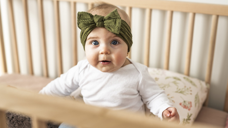 A baby with a green bow and blue eyes in a crib