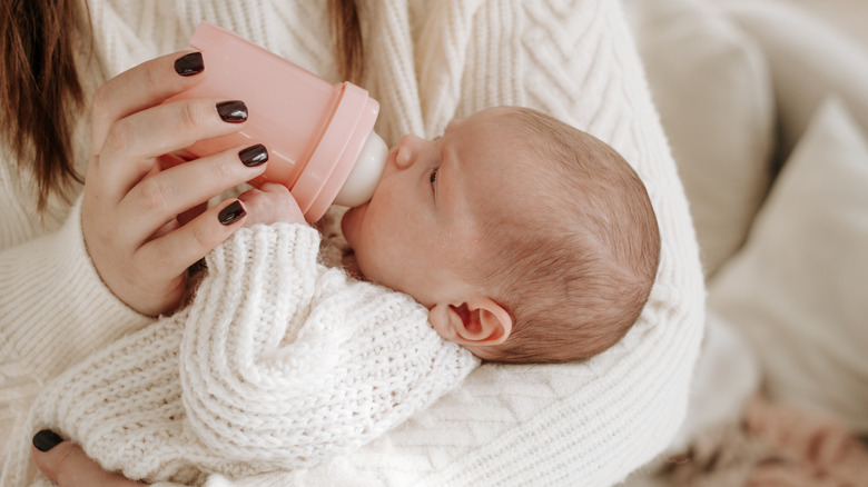 A baby being fed with a pink bottle