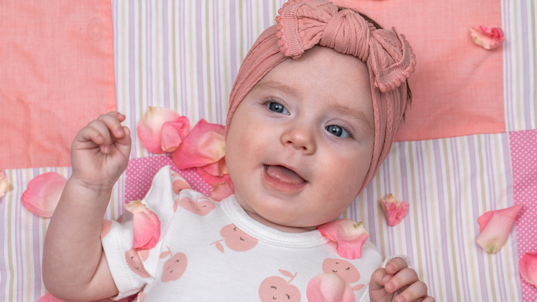 A baby wearing a pink head bow with petals scattered