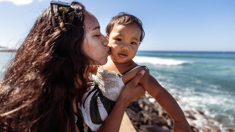 A mom kissing her baby in front of the ocean