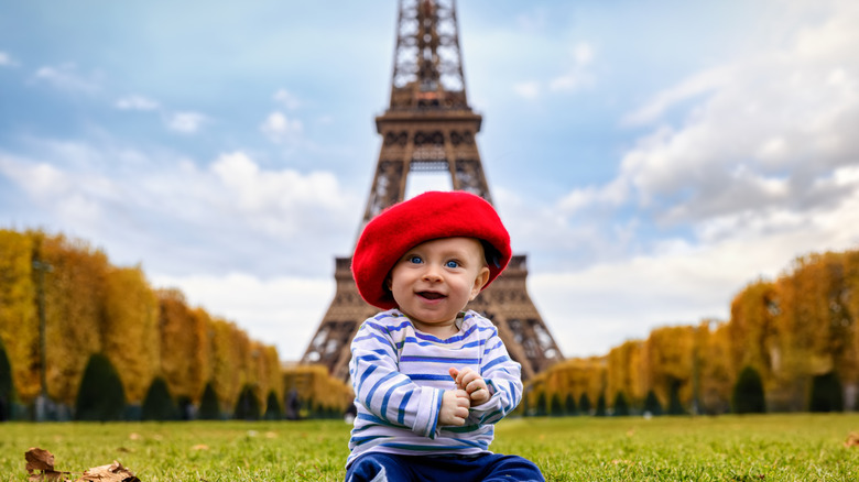 A baby wearing a French hat in front of the Eiffel Tower in Paris