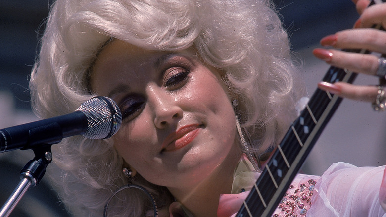Close up shot of Dolly Parton performing in 1978 next to a microphone playing a guitar.