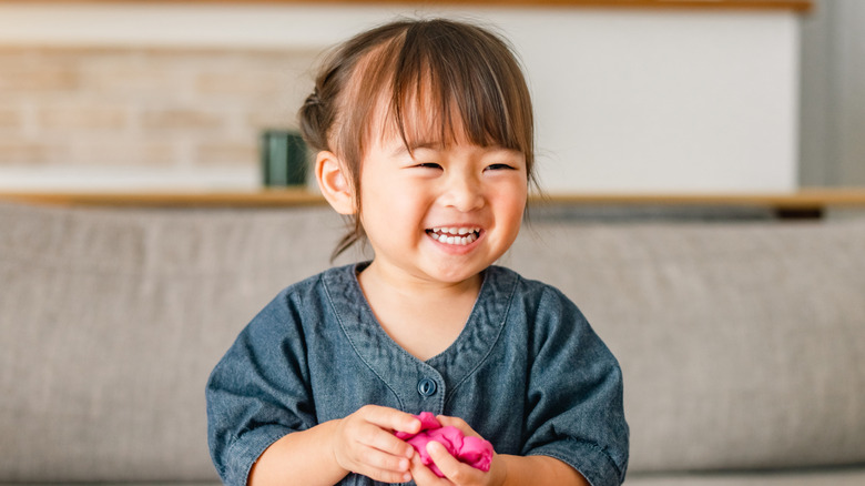 A laughing toddler holding play dough