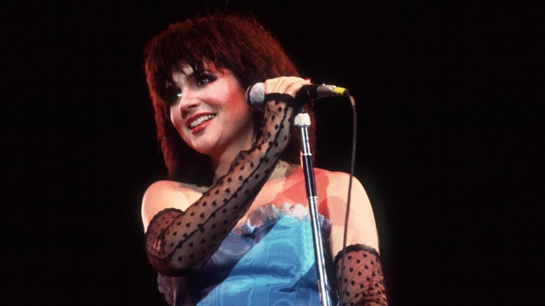 Linda Ronstadt wearing a blue strapless top and sheer fingerless gloves while performing in the '80s