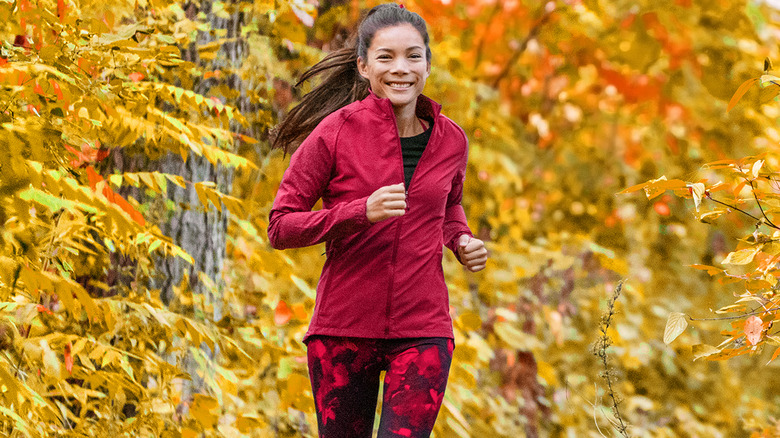 Woman running on path surrounded by autumn leaves