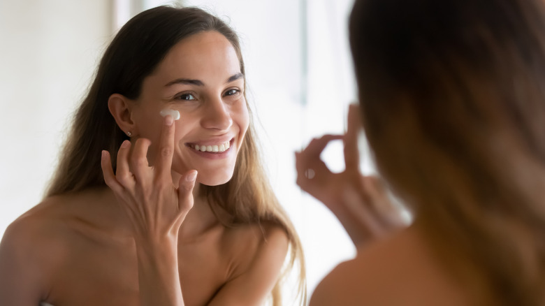 Woman applying moisturizer in mirror