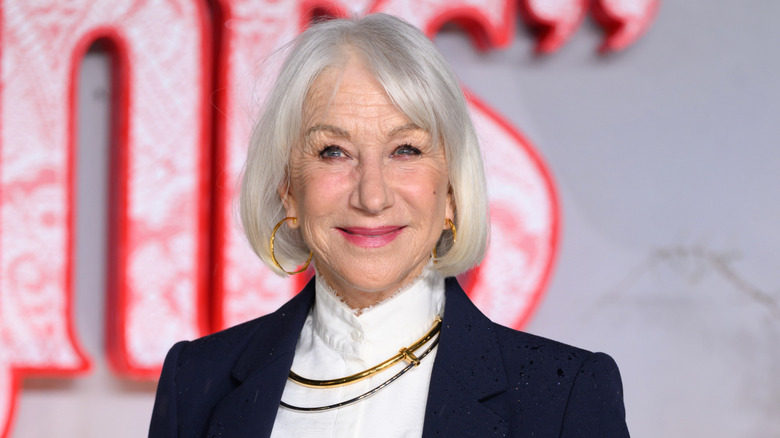 Actor Helen Mirren smiling and wearing hoop earrings and a blazer.