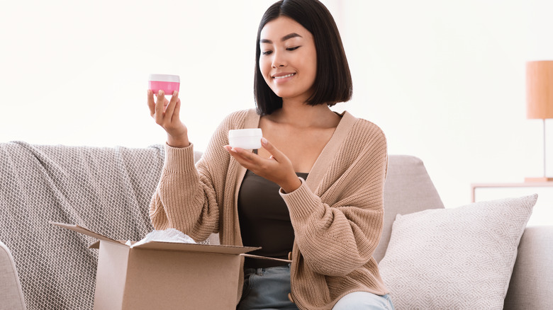 Woman holding up skincare from online shopping purchase