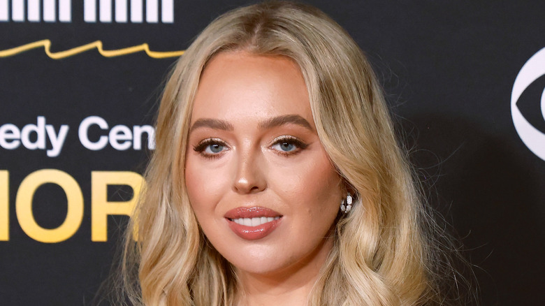 Tiffany Trump wearing peachy lip gloss posing in front of black background