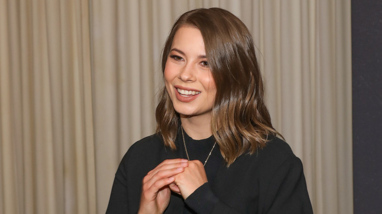 Bindi Irwin at an event wearing a black top with a gold necklace.