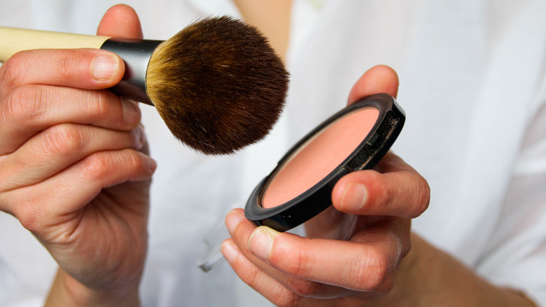 woman tapping blush onto brush