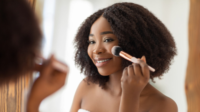 woman applying blush in mirror