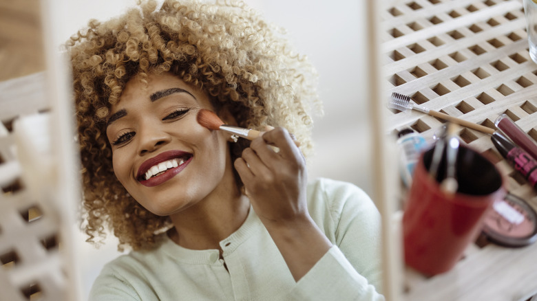 Woman applying blush to upper cheek