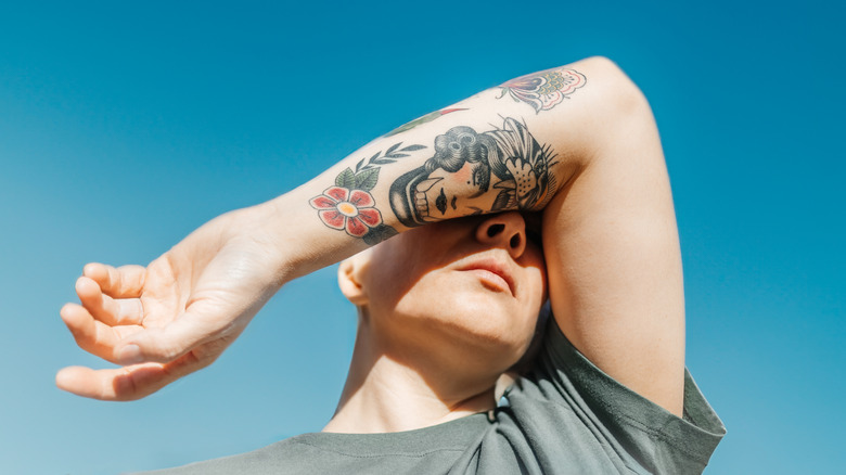 Person covering face with tattooed arm