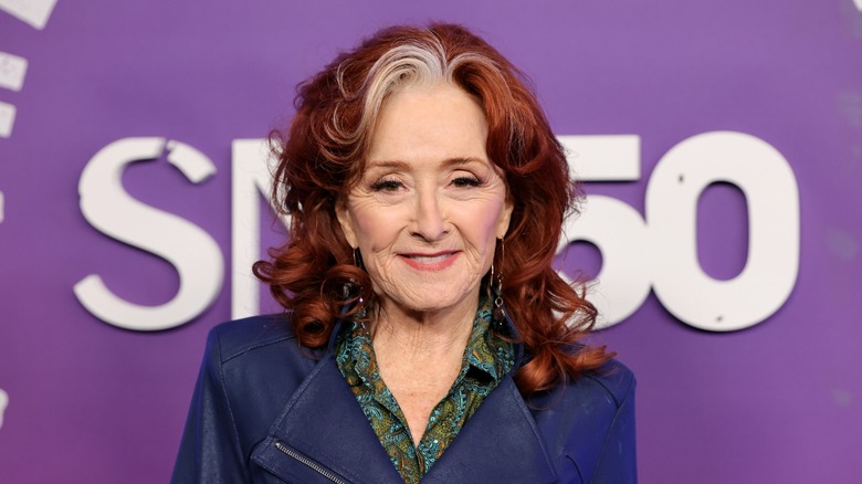 Bonnie Raitt shows off her gray streak and bright red curls with a blue jacket and collared shirt underneath while attending SNL50: The Homecoming Concert in New York City in 2025.
