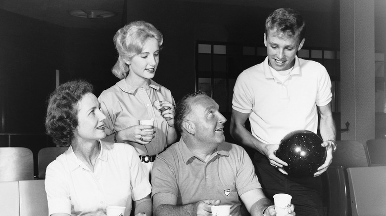 Teenagers bowling with their parents in the 1950s