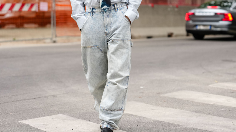 Close-up to someone's legs as they walk wearing acid wash jeans and a white shirt