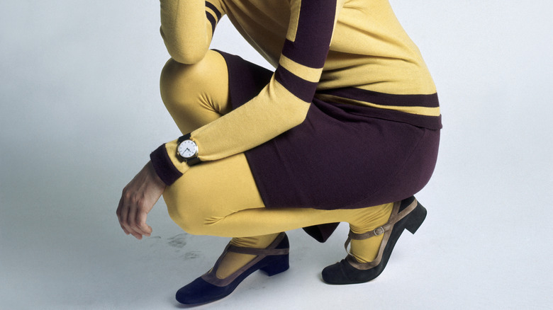 Close-up to a woman's legs as she wears yellow tights and a yellow-and-purple dress