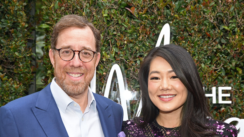 Rob Minkoff and Crystal Kung smile while posing together in front of green foliage backdrop