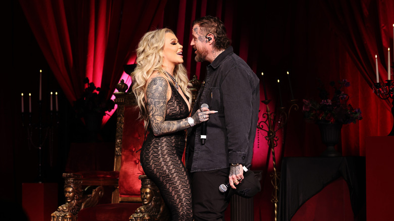 Bunnie Xo and Jelly Roll stand facing each other holding mics and wearing black outfits