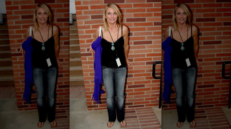 Cameron Diaz in jeans and a black top standing by a brick wall