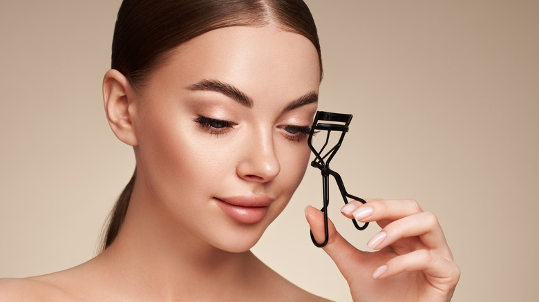 Woman holding eyelash curler up to face 