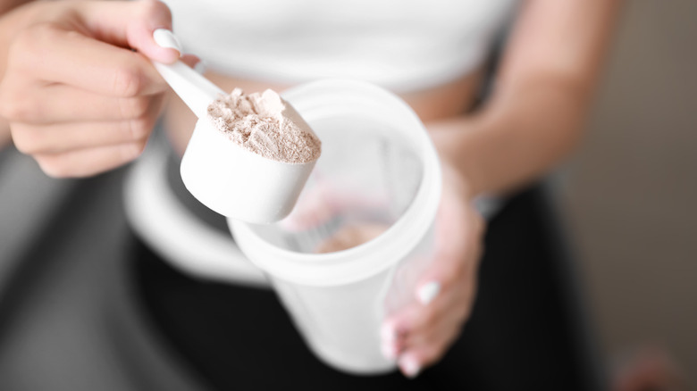 Woman holding scoop of protein powder from canister