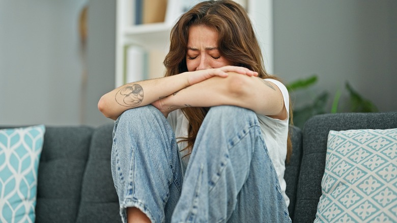 Woman alone crying while sitting on her sofa