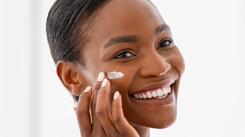 Woman applying skincare to cheeks while smiling 