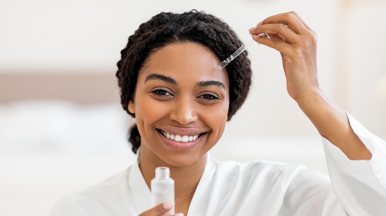 woman applying serum on face while smiling