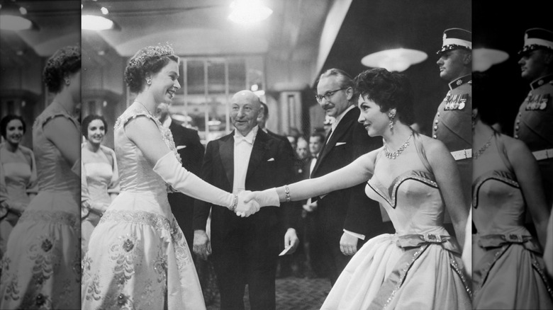 Gina Lollobrigida wearing a low-cut halter dress shaking hands with Queen Elizabeth.