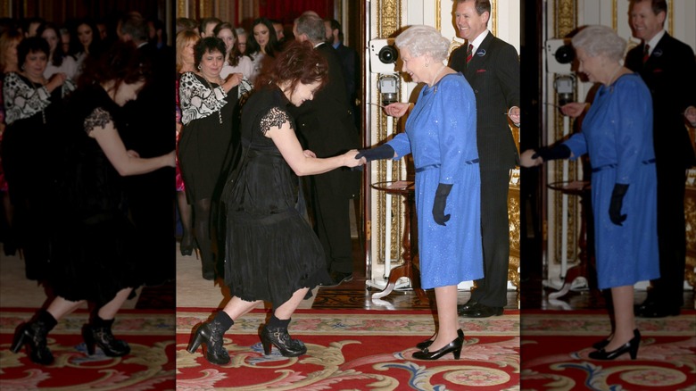Helena Bonham Carter curtsying in a black dress and boots shaking hands with Queen Elizabeth. wearing a blue dress.