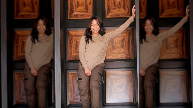 Angela Bassett posing in a brown outfit with her hand on the wall.