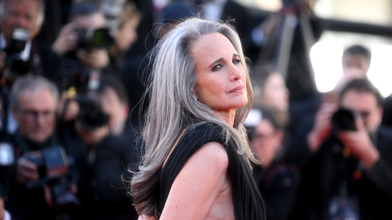Andie MacDowell on the red carpet wearing a black dress with long gray hair.
