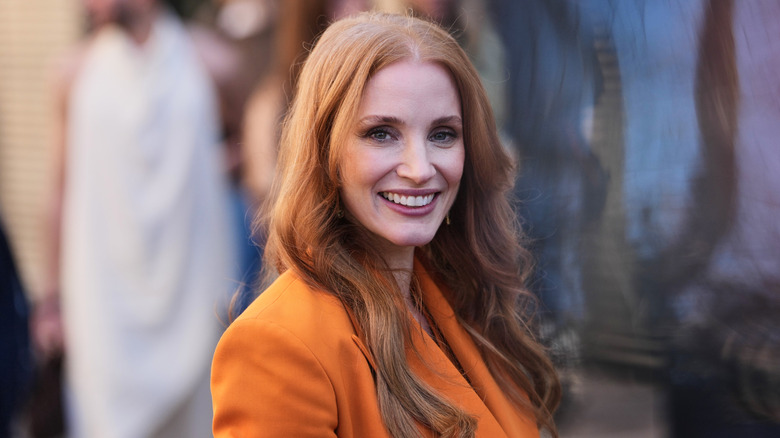 Jessica Chastain posing at an event wearing an orange blazer dress.