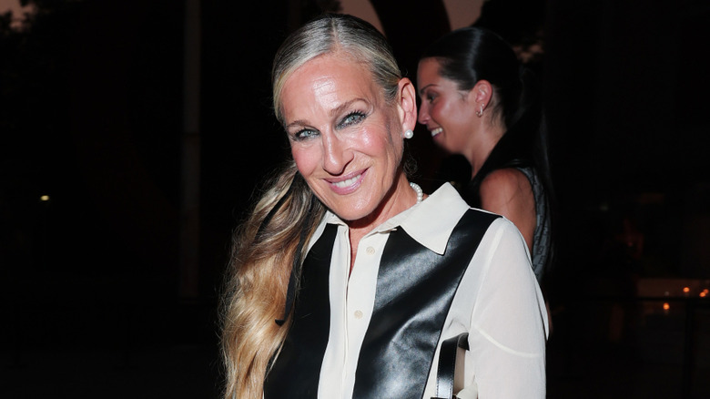 Sarah Jessica Parker posing at an event wearing a black-and-white top with her hair in a low ponytail.