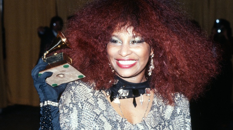 Chaka Khan is photographed with her signature red afro while smiling and holding a Grammy award