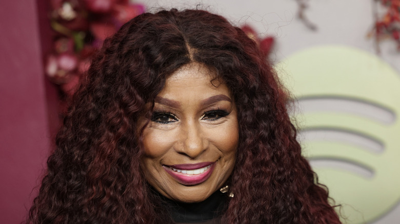 Chaka Khan poses on the red carpet with crimped hair and full-glam makeup featuring pink lipstick.