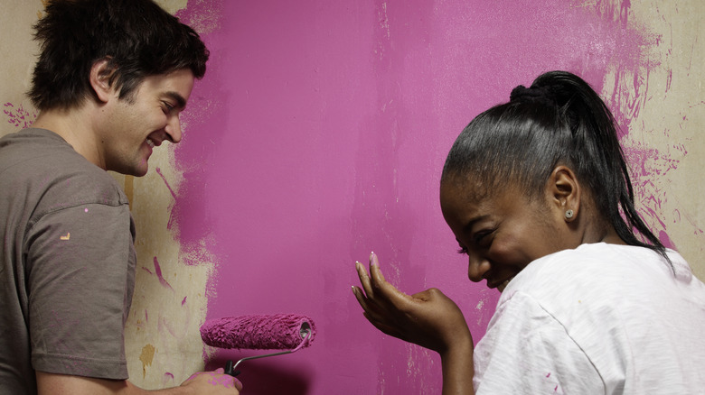 couple laughing and painting a wall pink