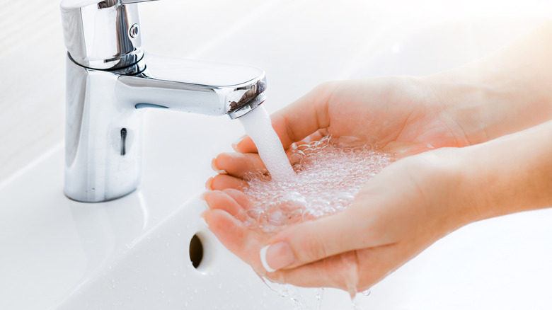 person washing hands with running tap water