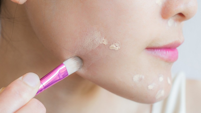 Woman applying concealer to chin