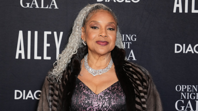 Phylicia Rashad smiles wearing a crystal necklace and a fur coat