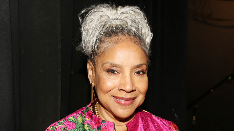 Phylicia Rashad smiles wearing her gray hair in a bun and a hot pink jacket