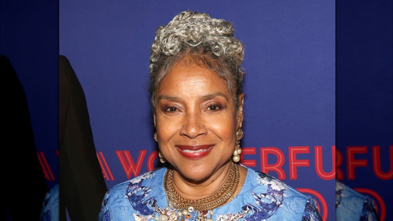 Phylicia Rashad smiles wearing a bun hairstyle and pearl earrings