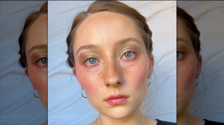 A person with freckles and radiant eye makeup posing for a picture